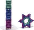 The Speks Unwind Gradient set features colorful magnetic balls in various shades of green, blue, and purple. One structure is a tall column formed from stacked beads, while another is a star-shaped construction showcasing the vibrant colors. Ideal for creative play and stress relief, these magnetic pieces can be arranged in numerous ways.