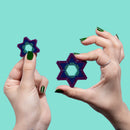 Two hands holding colorful star-shaped fidget toys made of small magnetic spheres. One star is larger and vibrant with gradient colors, while the other is smaller and shares a similar design. The background is a soothing mint green, emphasizing the playful nature of the toys.