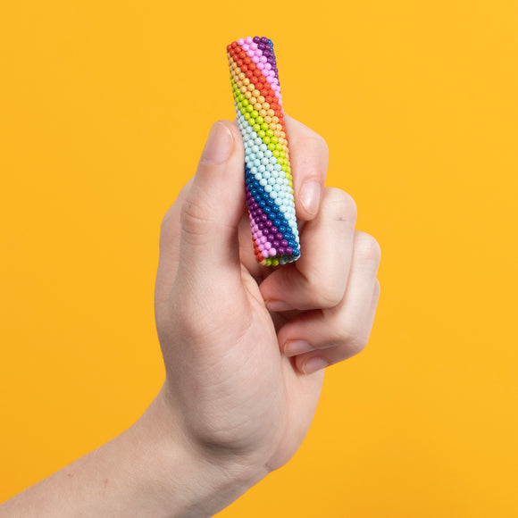 A hand holding a colorful fidget toy called Speks: Matte Spectrum. The toy features a vibrant design with a mix of rainbow colors, creating an engaging and tactile experience against a bright yellow background.