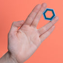 A hand holding a colorful hexagonal fidget toy made of magnetic beads. The toy is set against a vibrant orange background, showcasing its structure and design.