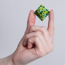 A hand holding a colorful geometric fidget toy made of small magnetic beads, shaped like a cube with green, yellow, and blue patterns. The toy appears playful and engaging, suitable for stress relief and creative manipulation.