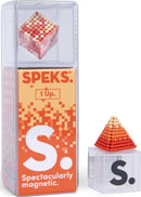 Speks Pixel 1 Up by SPEKS features a vibrant, magnetic construction set with colorful beads housed in a clear plastic case. The product displays a small pyramid structure made of the beads, showcasing creativity and playfulness in building unique shapes. The packaging emphasizes its strong magnetic properties, appealing to both kids and adults looking for tactile stimulation and stress relief.