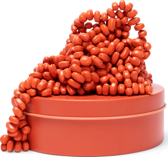 A pile of coral-colored, oval-shaped tactile beads spilling out from a matching sturdy container. The beads are designed for sensory play and creative activities, showcasing a vibrant shade of coral.