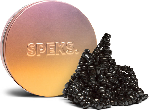 A circular tin can with a gradient metallic finish from gold to pink, labeled 'SPEKS.' Next to it, a pile of black, bead-like magnetic blocks is artistically arranged, showcasing their unique shape and texture. The product is designed for fidgeting and creative builds, providing a satisfying tactile experience.