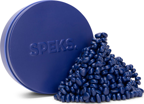 A round blue tin labeled 'SPEKS.' with a mound of small, glossy, blue speks spilling out. The speks are oval-shaped and densely packed, creating a playful and visually appealing display.