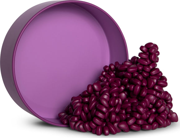 A circular purple tin with a matte finish is shown, partially filled with glossy, iridescent, kidney-shaped pieces resting on its side. The vibrant pieces are in various shades of deep purple and are scattered around the tin.