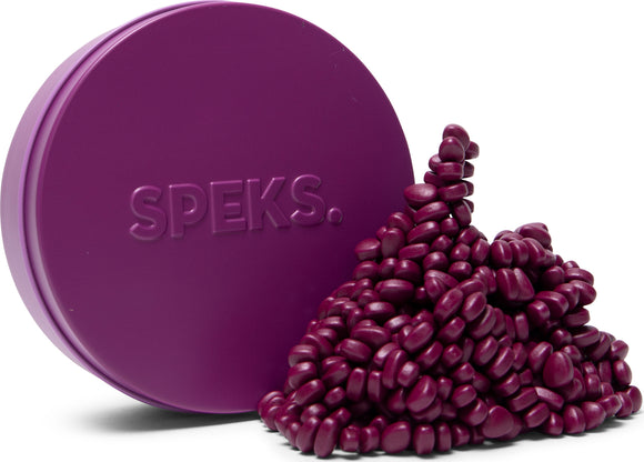 A round purple tin labeled 'SPEKS.' sits alongside a pile of small, glossy, purple beads that resemble pebbles. The arrangement showcases the vibrant color and unique shape of the beads, which are perfect for fidgeting and creative play.