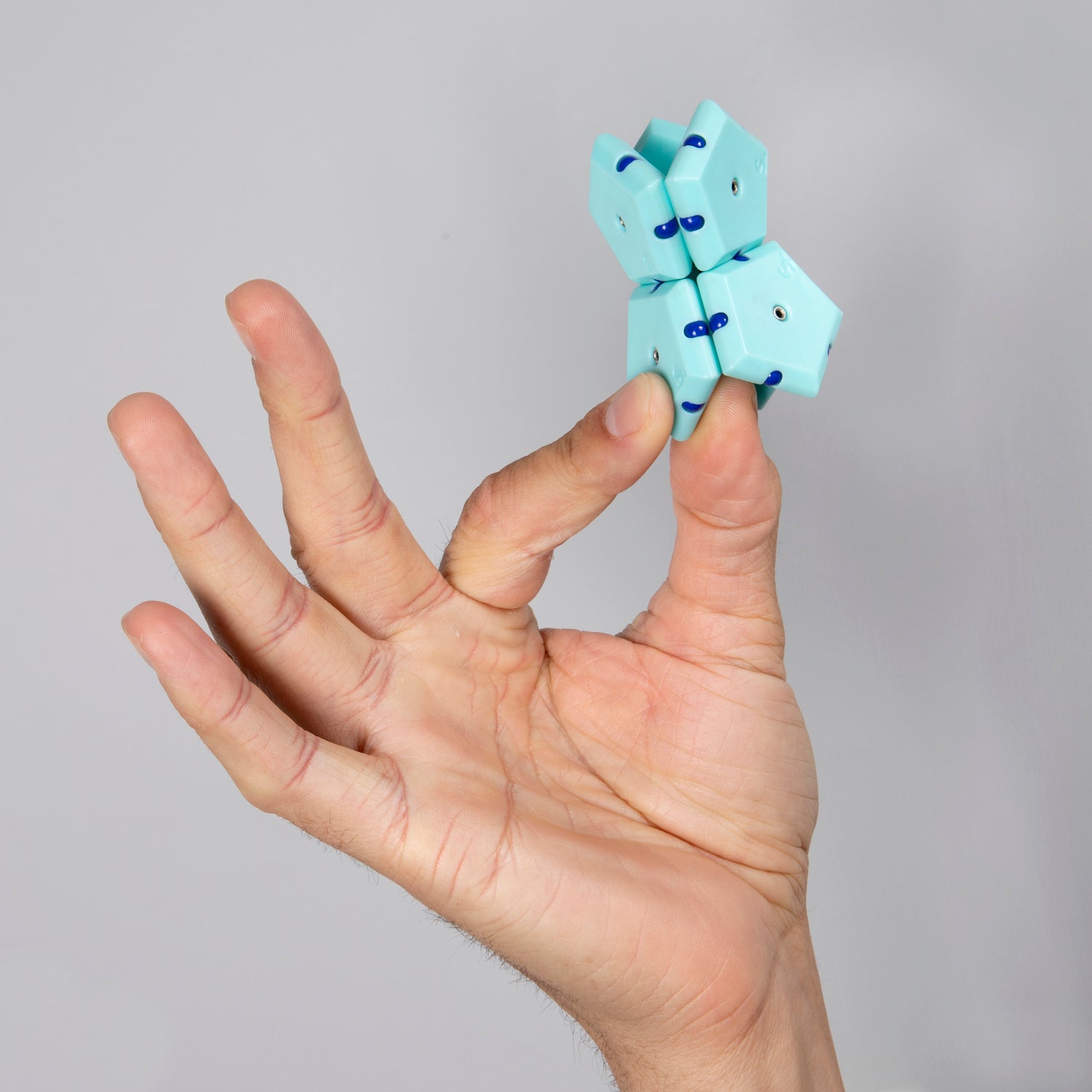 A hand holding the Speks Geode: Mile High, a colorful and engaging fidget toy. The fidget toy features multiple connected segments in light blue and dark blue, designed for fun and relaxation.