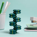 The Speks Geode: Monstera, a stacking puzzle featuring colorful interlocking pieces, displayed upright with a light aqua background. A white cup with pens and a stapler can be seen in the background, highlighting a fun and creative workspace environment.