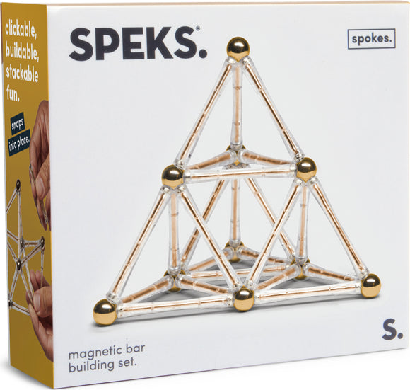 The Speks: Spokes Gold box showcases a magnetic bar building set, featuring a pyramid structure made from clear connectors and golden spheres. Hands are shown assembling the pieces, emphasizing the set's interactive and creative potential.