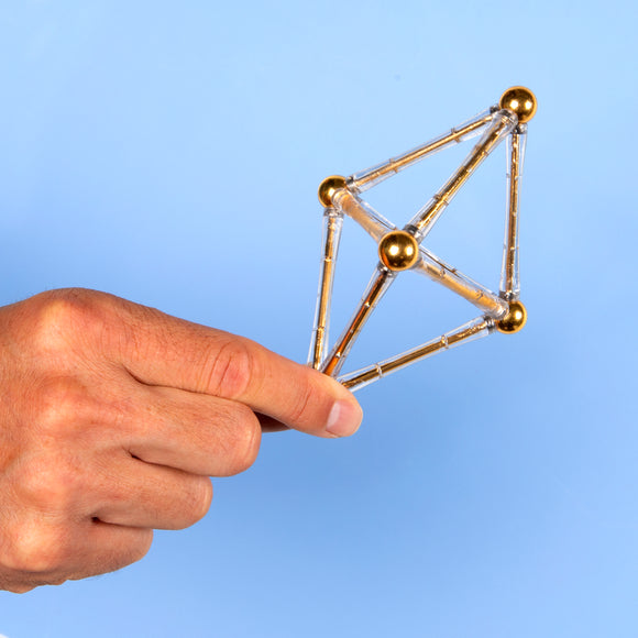 A person holding a geometric structure made of transparent and gold-colored pieces, showcasing the intricate design of the Speks: Spokes Gold. Perfect for stress relief and creativity.