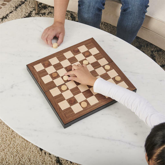 Two people playing a game of checkers on a deluxe wooden board. The board features alternating light and dark squares, with wooden checkers being moved by the players. The setting is a cozy living room with a marble table and a plush rug in the background.
