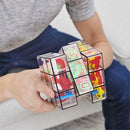A person holding the Perplexus Rubik's Fusion 3x3 mechanical puzzle by Spin Master Games. The puzzle features a transparent design with colorful pathways and obstacles inside. The individual is showcasing the puzzle while seated on a couch, with a casual outfit visible.