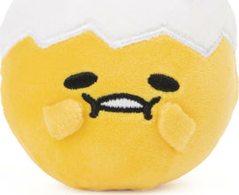 Gudetama Round Squishy Asst. 3 by GUND featuring a cute, squishy plush design of Gudetama, the lazy egg character, with a soft yellow body and white top. Its expression is relaxed, embodying a laid-back vibe perfect for fidgeting or collection.