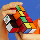 A person holding a Rubik's Tower, a 2x2x4 mechanical puzzle by Spin Master. The puzzle features vibrant colors, including red, green, yellow, orange, and white cubes, structured in a tower shape. The background is a solid blue, emphasizing the colorful design of the puzzle.