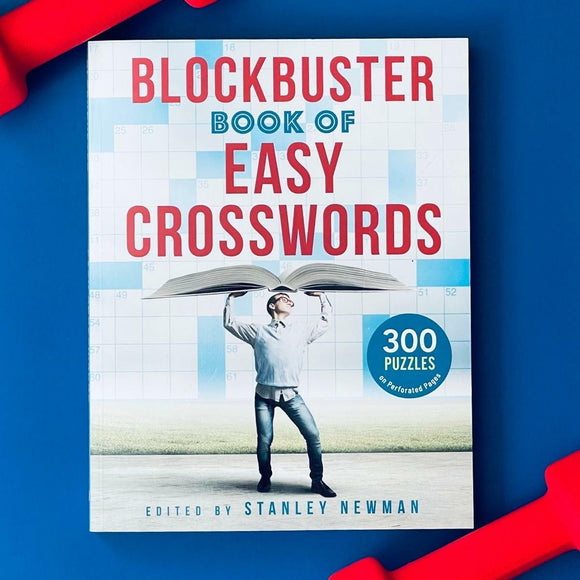 The Blockbuster Book of Easy Crosswords features a colorful cover with the title prominently displayed. A person is humorously holding the book open above their head, surrounded by a crossword puzzle theme. The cover mentions '300 puzzles on perforated pages,' highlighting its accessibility and fun.