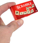 A person holding the World's Smallest Scrabble game by Super Impulse. The compact game features wooden letter tiles with images of the letters P, L, A, Y, S, W in a vibrant red box.