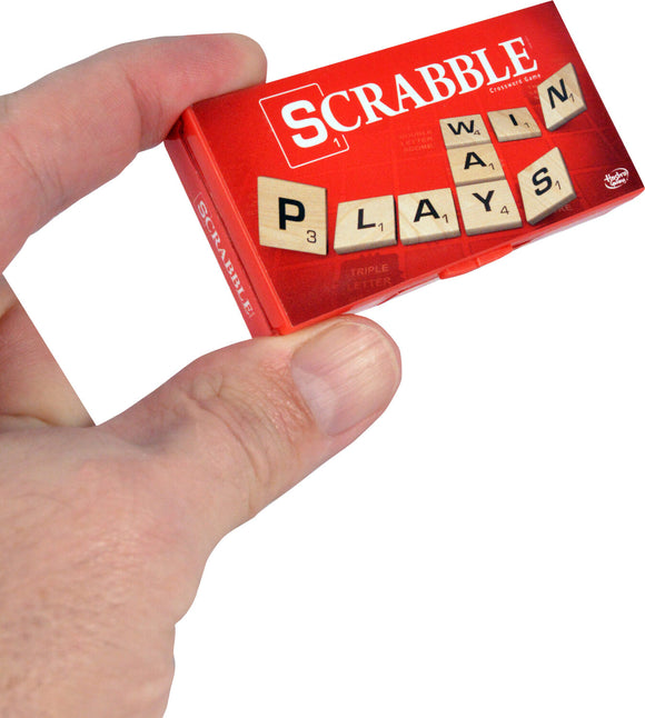 A person holding the World's Smallest Scrabble game by Super Impulse. The compact game features wooden letter tiles with images of the letters P, L, A, Y, S, W in a vibrant red box.