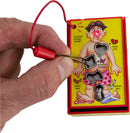 A close-up of the World's Smallest Operation game by Super Impulse, showing a hand using tweezers to carefully extract pieces from a cartoonish surgical figure with humorous ailments like 'butterflies in stomach' and 'broken heart.' The game features bright colors and a playful design.