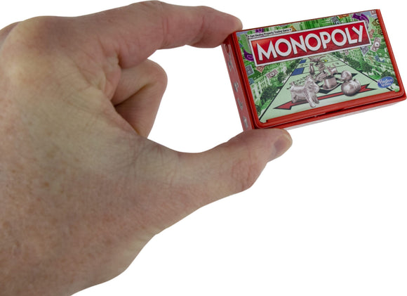 A person holding the World's Smallest Monopoly game, showing the tiny red box featuring the game's logo and Monopoly board artwork. The game is compact and fits in the palm of the hand.