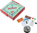 A compact version of Monopoly from Super Impulse, featuring a small red case with the game board visible. The board displays the iconic Monopoly layout with colorful properties and Chance/Community Chest cards. Also shown are game pieces, dice, and play money, all arranged around a quarter for scale.
