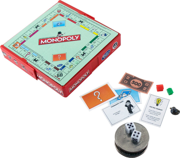 A compact version of Monopoly from Super Impulse, featuring a small red case with the game board visible. The board displays the iconic Monopoly layout with colorful properties and Chance/Community Chest cards. Also shown are game pieces, dice, and play money, all arranged around a quarter for scale.
