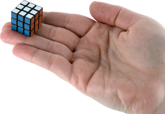 A person's hand holding the World's Smallest Rubik's Cube by Super Impulse, showcasing its compact size and vibrant colored squares. The cube fits comfortably in the palm, highlighting its mechanical puzzle design.