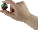 A hand holding the World's Smallest Rubik's Cube by Super Impulse. The cube is a miniaturized version of the classic puzzle, showcasing vibrant colors: green, red, yellow, and blue on its faces. The hand appears to be demonstrating the compact size of the cube, emphasizing its mechanical puzzle design.
