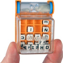 A person holding the World's Smallest Boggle game by Super Impulse. The game features a transparent cube with an orange base containing lettered dice inside, ready for word-finding fun. An hourglass timer is visible on the top, indicating it's a fast-paced game.