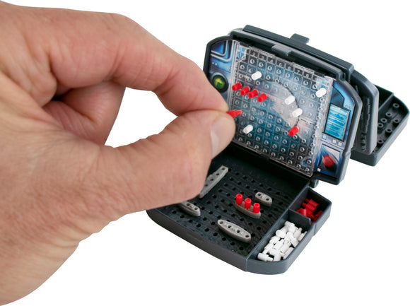 A close-up view of the World's Smallest Battleship game by Super Impulse, featuring a hand placing a red peg on the game board. The game is compact, showcasing a detailed grid with red and white pegs and small battleship pieces neatly stored in the base.