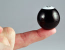 A person holding the World's Smallest Magic 8 Ball by Super Impulse on their fingertip. The black ball features a white top and is a miniature version of the classic fortune-telling toy, perfect for fun predictions.