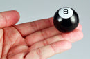 A person's hand holding the World's Smallest Magic 8 Ball by Super Impulse. The small black sphere features a white number '8' on top, resembling a classic Magic 8 Ball, designed for fun fortune-telling.