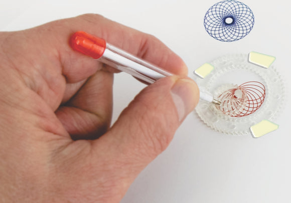 A person holding a pen over a spirograph tool, creating intricate spiral designs on paper. The spirograph kit includes colorful plastic components, featuring multiple geometric patterns.