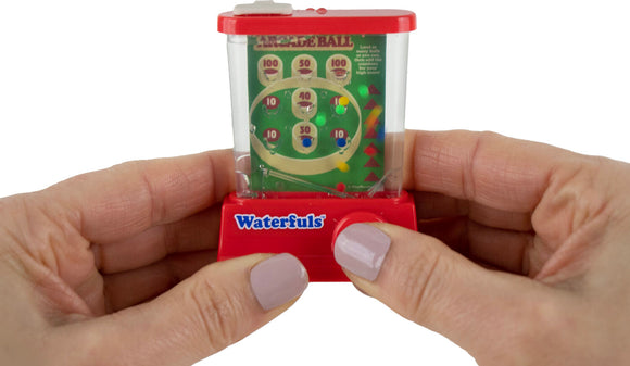 A person holding the World's Smallest Waterfuls toy, which features a clear plastic container filled with water and colorful balls. The front displays a scoring board with various point values marked. This handheld arcade game challenges users to land balls in scoring zones for fun and engagement.