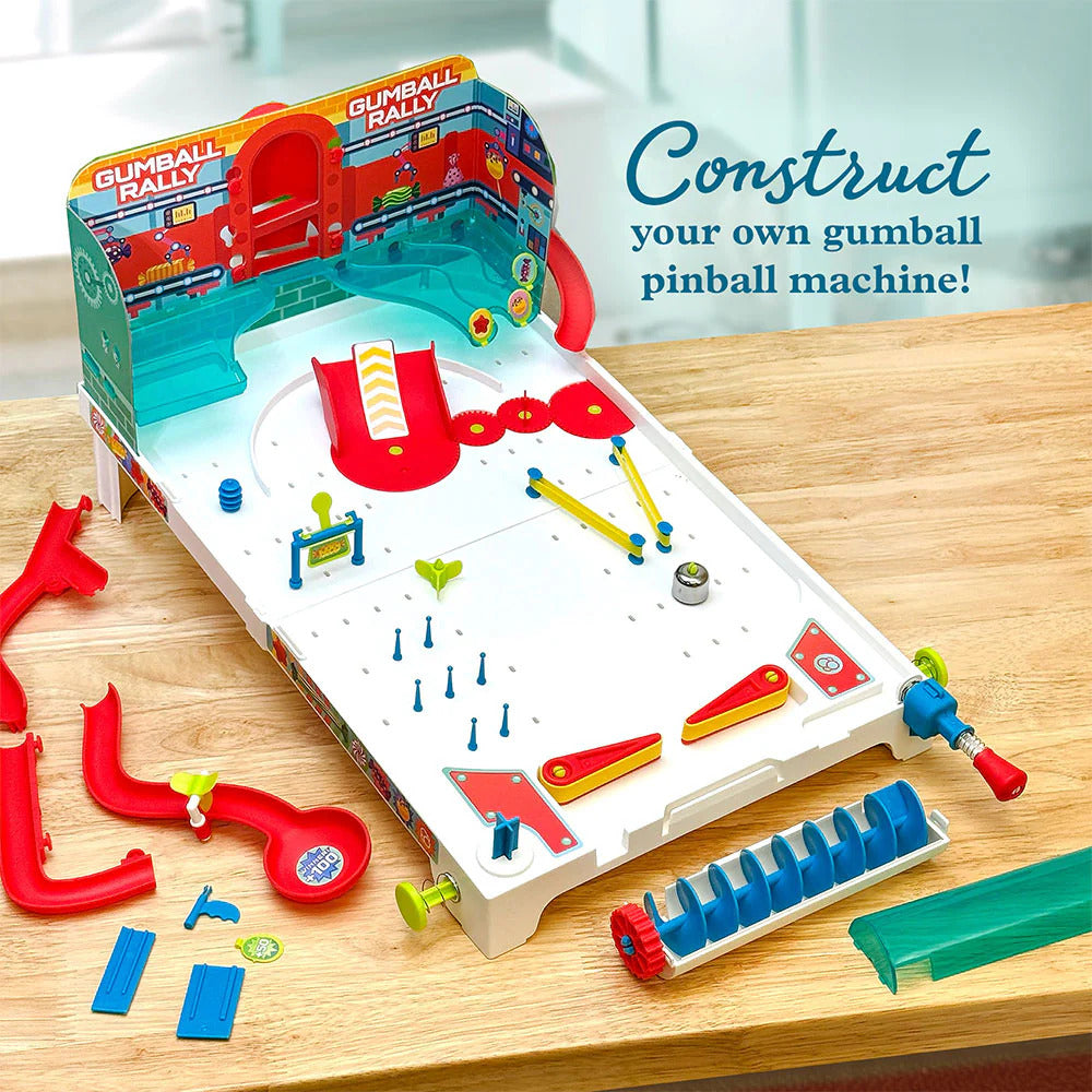 A colorful DIY gumball pinball machine kit from Thames & Kosmos, featuring vibrant ramps, levers, and gumball elements. The setup includes gumballs and construction pieces laid out on a wooden table, inviting users to build and play.