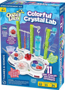 Ooze Labs Colorful Crystal Lab DIY kit by Thames & Kosmos features vibrant packaging showcasing 11 shiny crystal experiments. The kit includes various crystal forming ingredients and tools organized on a table station. Colorful, fluffy crystals are displayed in containers, and emphasizes STEM learning for ages 6 and up.