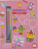 A colorful DIY kit called Sweat Treats Shrinkies by Tiger Tribe. The design features various adorable, cartoonish food characters, including ice cream cones, a cupcake, a cactus, and rainbow elements. The kit includes colored pencils for drawing and shrinking the designs, along with accessories like a keyring and strings. The vibrant pink packaging ensures an engaging crafting experience for children aged 5 and above.