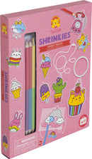 Tiger Tribe Sweat Treats Shrinkies DIY kit. The packaging features colorful illustrations of ice cream cones, cupcakes, and cute animals. Includes colored pencils for customization. Ideal for creating fun, whimsical charms and keychains.