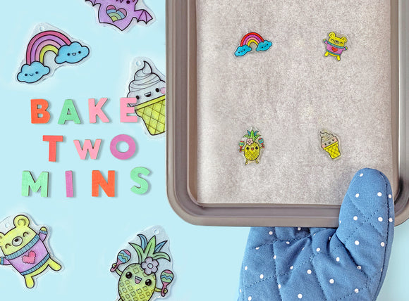 A colorful DIY kit titled 'Sweat Treats Shrinkies' by Tiger Tribe. The image shows fun, whimsical designs like a rainbow, ice cream cone, and pineapple shrinky dinks on a baking tray, with the words 'BAKE TWO MINS' in vibrant letters and a blue oven mitt holding the tray.