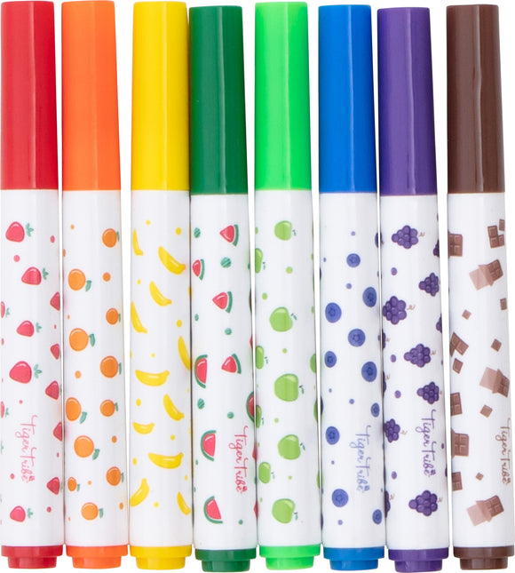 A set of eight vibrant scented markers by Tiger Tribe, featuring colorful caps in red, orange, yellow, green, blue, purple, and brown. Each marker has fun fruit-themed designs on the barrel, including strawberries, oranges, bananas, watermelons, green apples, blueberries, grapes, and chocolate pieces.