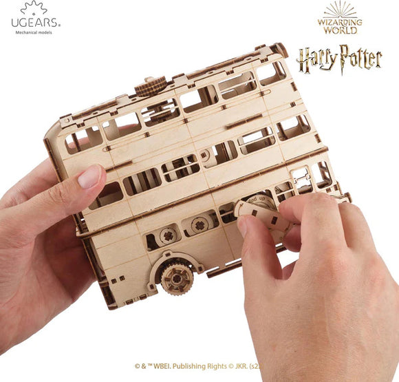 A person holding a detailed wooden model of the Knight Bus from Harry Potter. The model features intricate cut-outs and mechanisms and is part of the UGears 3D DIY kit. It's designed for enthusiasts who enjoy mechanical puzzles.