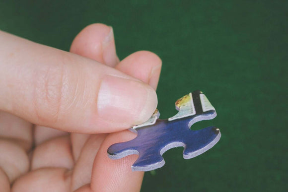 A person holding a colorful jigsaw puzzle piece featuring a blue background and a partial image of a scenic location, suitable for a jigsaw puzzle themed around New England.