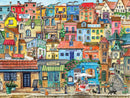 A vibrant jigsaw puzzle titled 'Seaside Village' by White Mountain Puzzles, featuring a charming coastal scene. The image displays colorful houses and shops, including a bakery, fish market, and a cafe with outdoor seating. Details include vacation rental signs, decorative flowers, and friendly animals, creating a lively and inviting atmosphere of a seaside town.