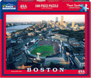 A vibrant jigsaw puzzle featuring an aerial view of Boston's Fenway Park during a game. The image showcases the historic ballpark surrounded by the Boston skyline and the Charles River, highlighting the energetic atmosphere of baseball season. The puzzle consists of 500 larger pieces, designed for easier handling and assembly, perfect for both puzzle enthusiasts and casual hobbyists.