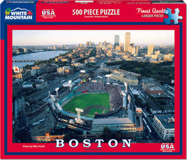 A vibrant jigsaw puzzle featuring an aerial view of Boston's Fenway Park during a game. The image showcases the historic ballpark surrounded by the Boston skyline and the Charles River, highlighting the energetic atmosphere of baseball season. The puzzle consists of 500 larger pieces, designed for easier handling and assembly, perfect for both puzzle enthusiasts and casual hobbyists.