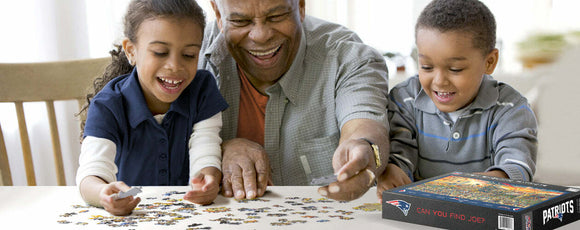 A joyful scene featuring a grandfather and two children engaged in assembling a New England Patriots jigsaw puzzle. The table is scattered with colorful puzzle pieces as they share smiles and laughter, with the puzzle box displaying 'Can You Find Joe?' prominently on the side.