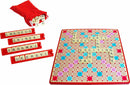 Scrabble game by Winning Moves displayed with a red drawstring bag containing letter tiles, four tile racks, and the game board featuring various words arranged on a colorful grid. The board includes double and triple letter and word score tiles, enhancing word game strategy.