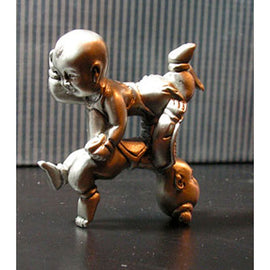 A unique mechanical puzzle titled 'Impossible Children' by John Bottoms. The sculpture features intricately crafted silver figures resembling children, intertwined in a complex design that creates an engaging three-dimensional puzzle. Each figure showcases fine detail, emphasizing the craftsmanship involved in this thought-provoking piece.