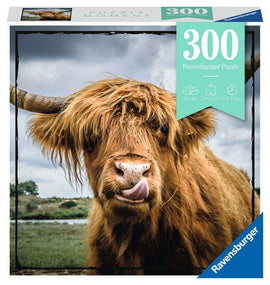 Ravensburger Jigsaw Puzzle titled 'Puzzle Moments: Highland Cattle' featuring a close-up image of a Highland cow with long, shaggy fur and large horns, licking its nose. The puzzle contains 300 pieces and emphasizes a relaxing and enjoyable experience.