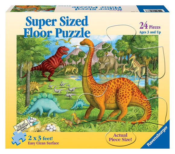 A colorful jigsaw puzzle box featuring a prehistoric landscape with various dinosaurs including a tall, spotted dinosaur, alongside a red T-rex and other species. The puzzle is designed for ages 3 and up and measures 2 x 3 feet. It contains 24 large pieces for easy handling, labeled with 'Actual Piece Size!' and 'Easy Clean Surface.'